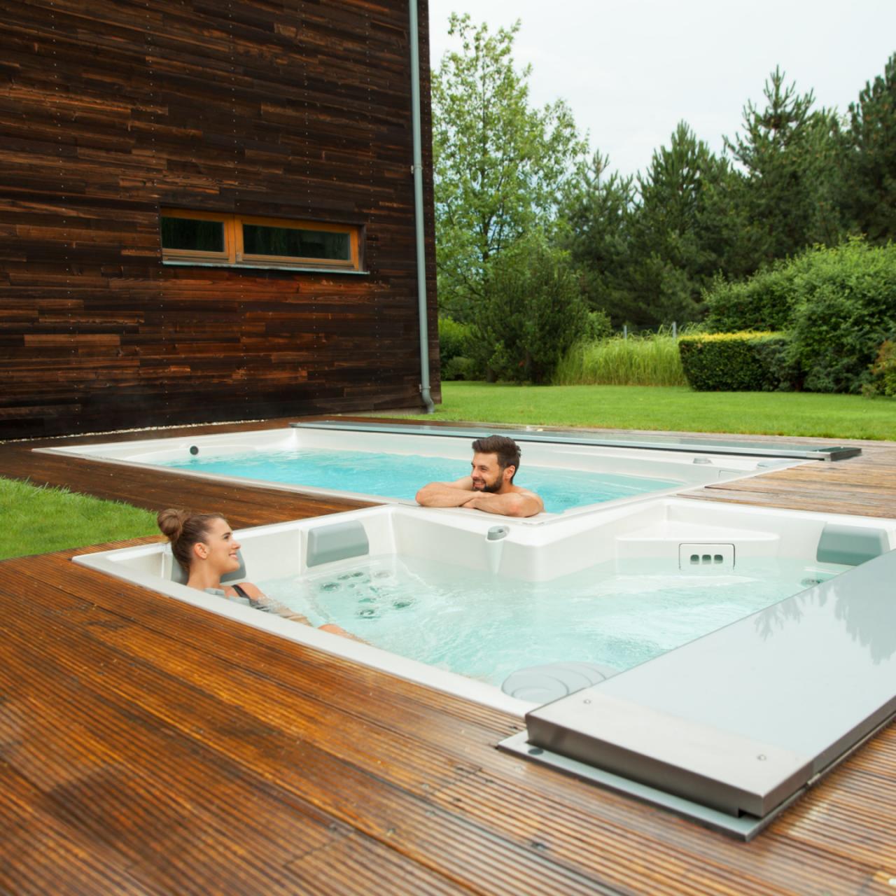Pāris atpūšas āra USSPA spa un peldbaseinos, kas uzstādīti uz koka terases.